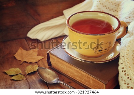 Cup of tea with old book, autumn leaves and a warm scarf on wooden table 