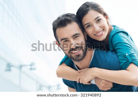 Closeup shot of young man carrying young woman on his back. Happy smiling couple looking at camera. Happy couple putdoor having fun piggyback in love.
