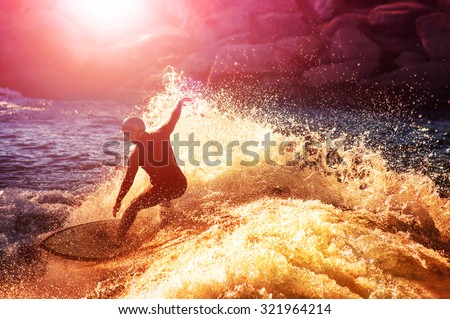 into the sun photo of a surfer riding a wave in a full wet suit toned with a retro vintage instagram filter app or action effect (SHALLOW DOF and long shutter speed action shot)  Royalty-Free Stock Photo #321964214