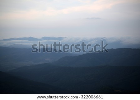 Beautiful spaciousness landscape view from high hill top on many mountain humps with deep green forests and cloudy grey blue sky on natural background, horizontal picture