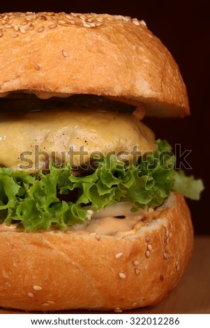 Big tasty appetizing fresh burger of green lettuce red tomato cheese and bacon slice meat cutlet and white bread bun with sesame seeds closeup, vertical picture