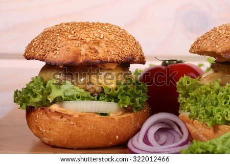 One big tasty appetizing fresh burger of green lettuce red tomato cheese bacon slice meat cutlet violet onion and white bread bun with sesame seeds on wooden table closeup, horizontal picture