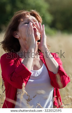 Hay fever allergies - sick middle age woman with tickling nose sneezing in the middle of dry meadow,natural summer daylight