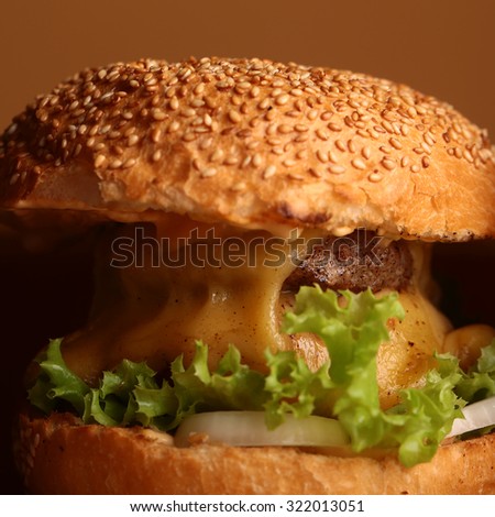 Big tasty appetizing fresh burger of green lettuce red tomato cheese and bacon slice meat cutlet and white bread bun with sesame seeds closeup, square picture