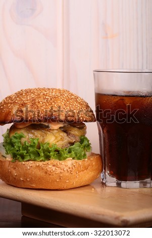 Big tasty appetizing fresh burger of green lettuce red tomato cheese and bacon slice meat cutlet and white bread bun with sesame seeds and glass of cola, vertical picture