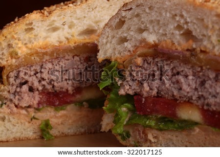 Closeup of one big tasty appetizing fresh burger of green lettuce red tomato cheese and bacon slice meat cutlet and white bread bun with sesame seeds cut on two half, horizontal picture