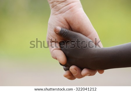 Beautiful Peace Symbol - White Woman Black Child Holding Hands. African Peace Symbol. White woman holds hands with a little native African girl, in Bamako, Mali.  Royalty-Free Stock Photo #322041212