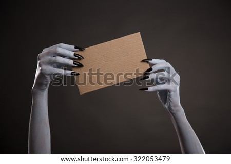 White witch hands with black nails holding blank cardboard, Halloween theme 