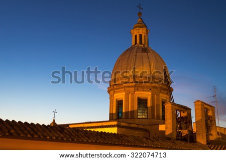 Church dome with a cross and bells lit by reflectors against dark blue evening sky