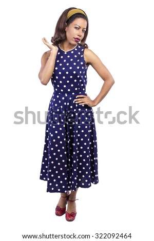 Black female wearing a blue vintage polka dot dress on a white background.  Her hairstyle has curls and she is wearing a pearl necklace.
