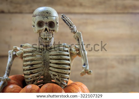 Skeleton is saluting on pumpkin and blur background.