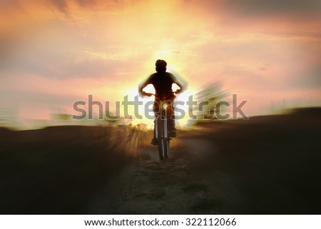 blurred image, silhouette of a boy on a bicycle, with rolling hills on the background of golden sunset 