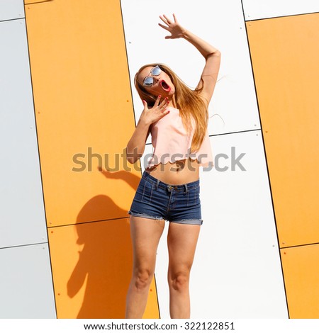 Trendy fashionable girl emotionally jumping on the background color of orange wall. Positive modern hipster girl joyfully jumps