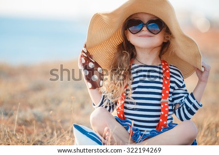 Pretty little girl in a striped dress and hat relaxing on the beach near sea, summer, vacation, travel concept. smiling cute little girl on beach vacation. Baby girl in hat and sun glasses on beach Royalty-Free Stock Photo #322194269