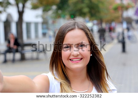 Smiling teen girl taking a selfie photo in an urban street 