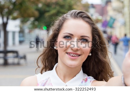 Smiling braces teeth teen girl taking a selfie photo in an urban street 