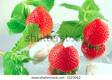 Fresh chilled strawberries with whipped cream and mint on a reflective background with a shallow depth of field