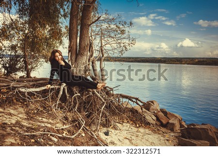 Beautiful young girl sitting on a rock by the river