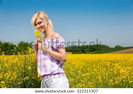 Young blond girl holding flowers surrounded by beautiful sunny yellow flower field