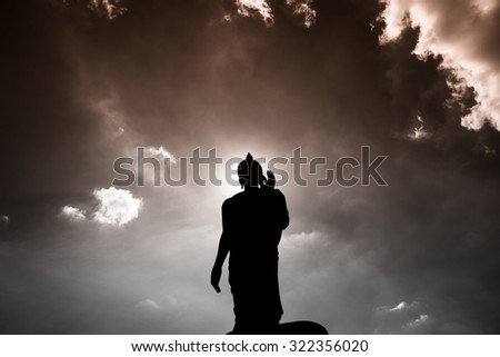 Buddha statue ok sign post bottom view with dark silhouette with deep clear blue sky with few clouds and white light glowing