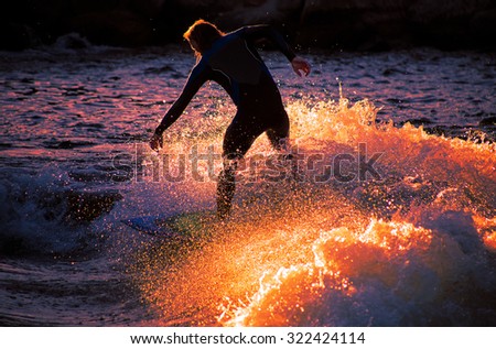 male surfer riding a wave in early sunrise or late sunset with a slower shutter speed to catch heavy water motion for effect of image with a toned instagram filter