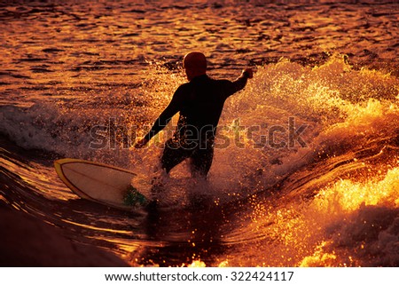 male surfer riding a wave in early sunrise or late sunset with a slower shutter speed to catch heavy water motion for effect of image with a toned instagram filter