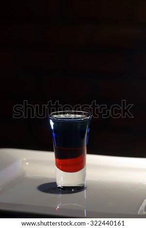 Closeup photo of one colorful twolevelled alcoholic shot cocktail red and blue colors in drinking glass standing on white plate on black background, vertical picture