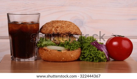 One big tasty appetizing fresh burger of green lettuce red tomato cheese bacon slice meat cutlet violet onion and white bread bun with sesame seeds on wooden table and cola, horizontal picture