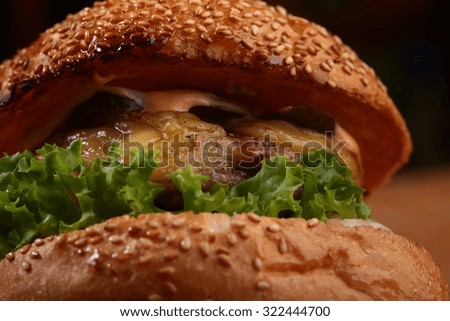 Big tasty appetizing fresh burger of green lettuce red tomato cheese and bacon slice meat cutlet and white bread bun with sesame seeds closeup, horizontal picture