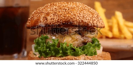 One big tasty appetizing fresh burger of green lettuce cheese bacon slice meat cutlet and white bread bun with sesame seeds and potato chips on wooden table closeup, horizontal picture