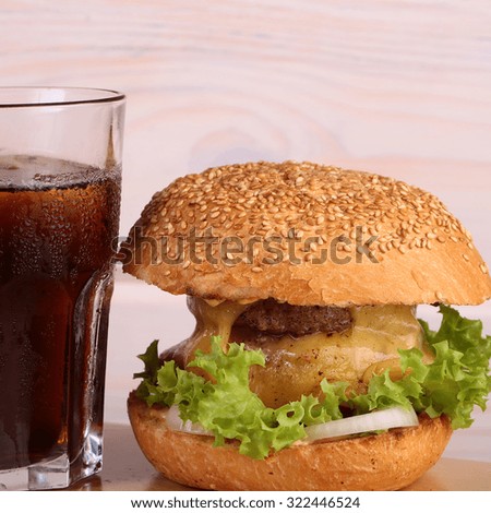 Big tasty appetizing fresh burger of green lettuce red tomato cheese and bacon slice meat cutlet and white bread bun with sesame seeds and glass of cola, square picture