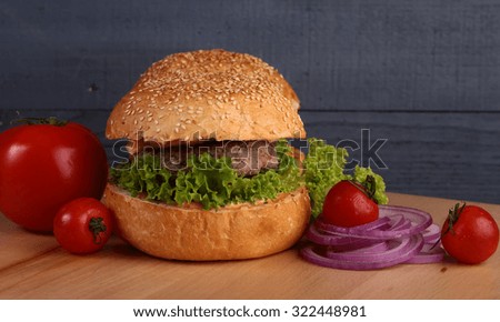 Big tasty appetizing fresh burger of green lettuce cheese bacon slice meat cutlet and white bread bun with sesame seeds and potato chips on wooden table closeup, horizontal picture