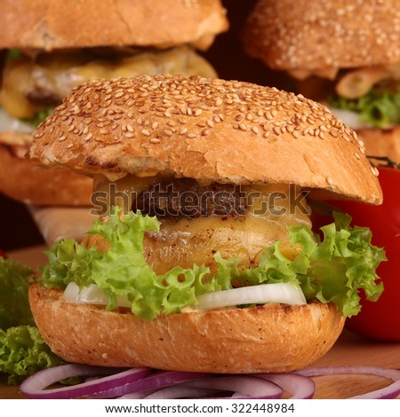 Big tasty appetizing fresh burgers of green lettuce red tomato cheese and bacon slice meat cutlet and white bread bun with sesame seeds closeup, square picture