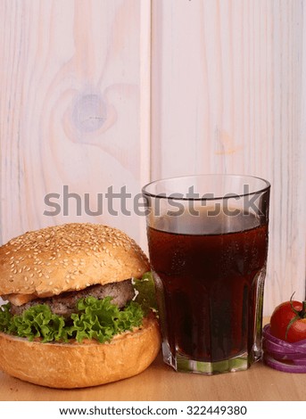 Big tasty appetizing fresh burger of green lettuce bacon slice meat cutlet and white bread bun with sesame seeds on wooden table and cola, vertical picture