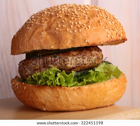 One big tasty appetizing fresh burger of green lettuce red tomato cheese and bacon slice meat cutlet and white bread bun with sesame seeds closeup, square picture