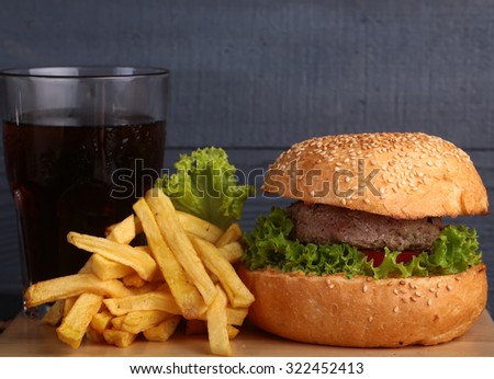 One big tasty appetizing fresh burger of green lettuce red tomato cheese and bacon slice meat cutlet and white bread bun with sesame seeds with cola and potato chips, horizontal picture