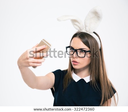 Portrait of a beautiful woman with bunny ears making selfie photo on smartphone isolated on a white background