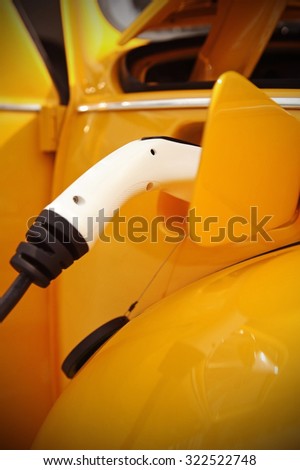 Vignetted shot with an electric plug in connected and charging a classic car