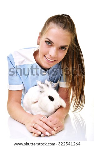 Smiling vet holding up and examining cute white rabbit at pets' clinic.