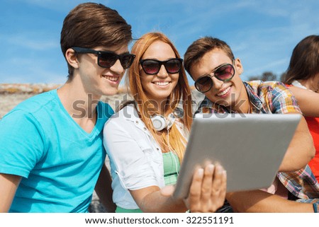 friendship, leisure, summer, technology and people concept - group of smiling friends with tablet pc computer sitting outdoors