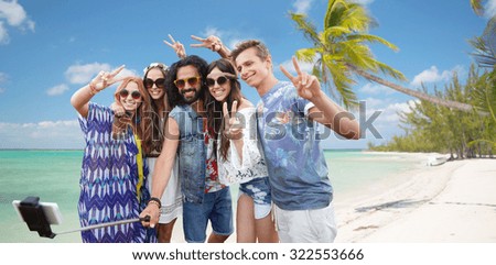 summer vacation, travel, technology and people concept - smiling young hippie friends in sunglasses taking picture by smartphone on selfie stick and showing peace gesture over beach background