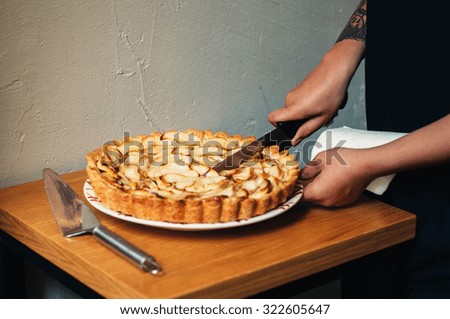 homemade delicious traditional apple pie with caramel on a plate on wood table and white background cool girl with tattoo slicing with knife trendy style