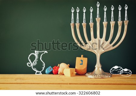 image of jewish holiday Hanukkah with drawing menorah candles (traditional Candelabra), donuts and wooden dreidels (spinning top) over chalkboard background
