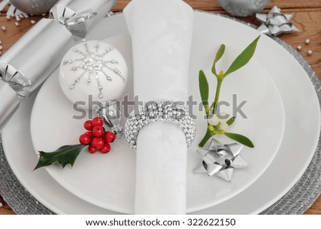Christmas holiday dinner place setting with plates, napkin,  bauble decorations, holly and mistletoe over oak background.