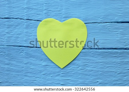 Blank yellow paper note with heart shape on grunge blue wooden background with copy space