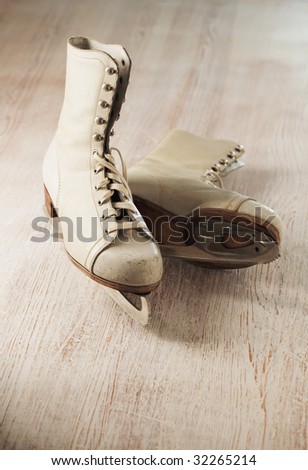Old and worn women's white ice skates on wooden surface