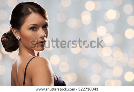 people, holidays, jewelry and luxury concept - woman face with diamond earring over lights background