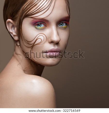 Beautiful girl with bright colored makeup and wet strands of hair on the face. Creative image. Picture taken in the studio.