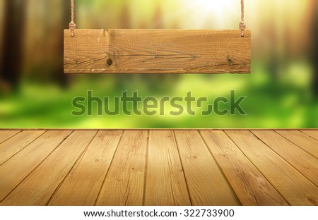 Wood table with hanging wooden sign on green forest blurred background