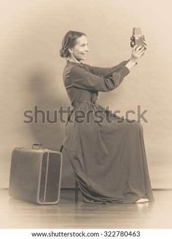 Woman retro style long dark gown old suitcase and camera taking picture, vintage photo sepia tone